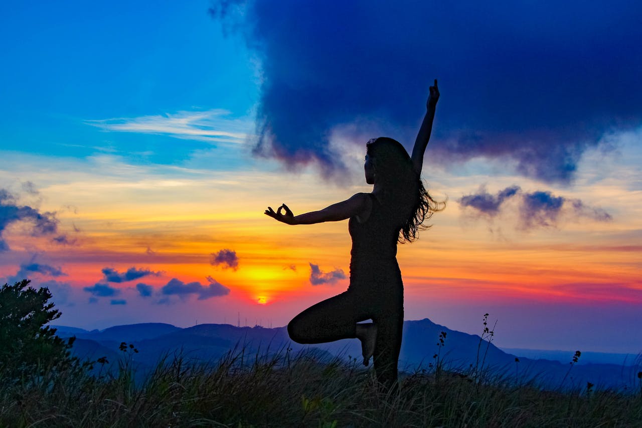 Woman practicing yoga at sunset in Panama, silhouetted against a vibrant sky and mountainous backdrop.